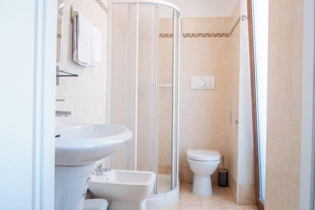 Et moderne badeværelse med glasbrusekabine, et væghængt håndvaskarrangement og toilet.