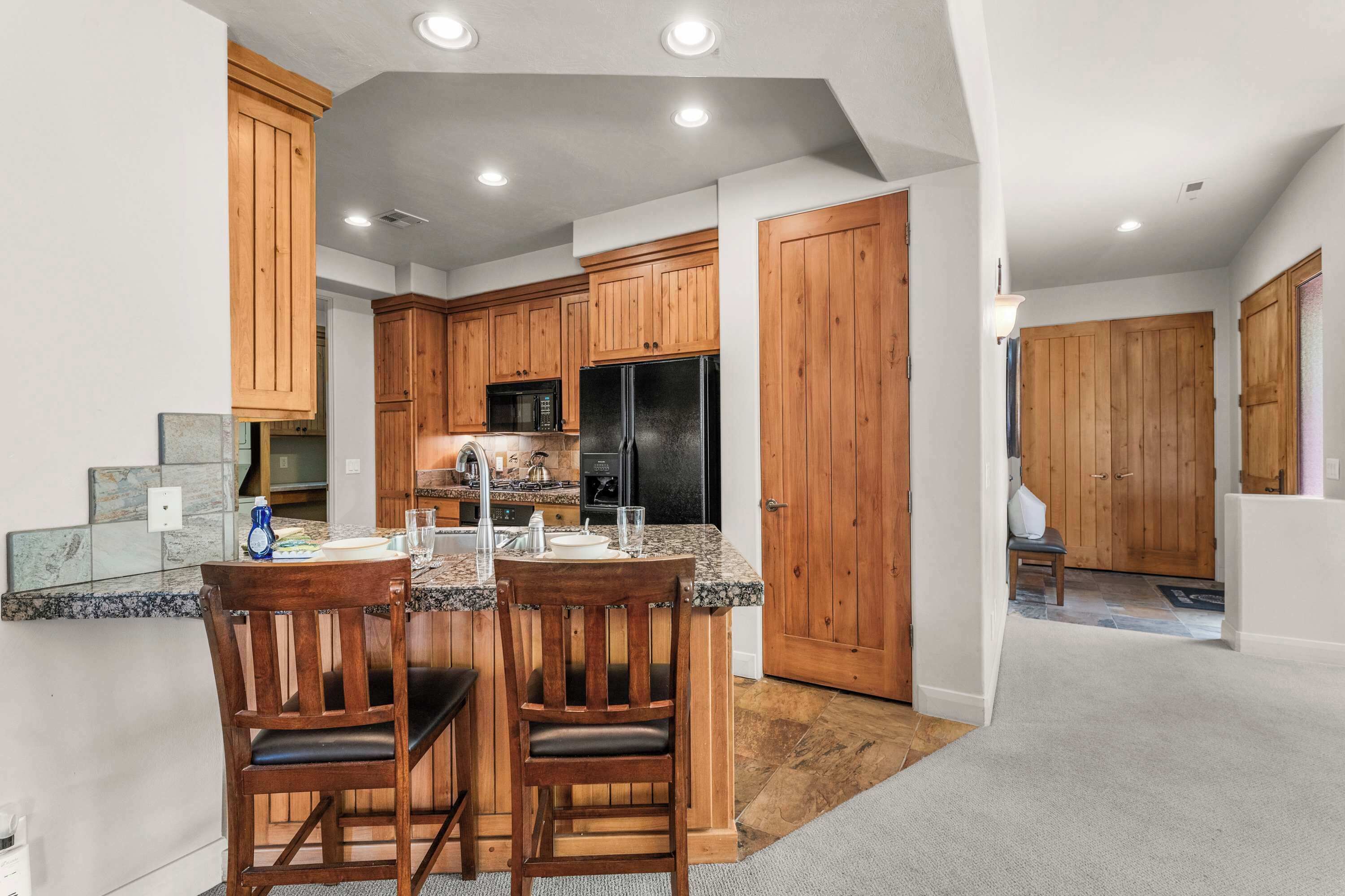 A kitchen with wooden cabinets, a granite countertop, and a dining area with two chairs.