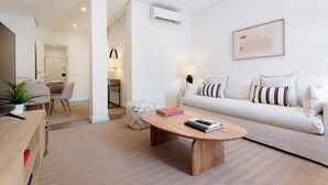 A modern living room with a sofa, coffee table, and a TV on a wooden stand. There is a dining area in the background with a table and chairs. - Genteel Home Abada Terrace (Madrid)