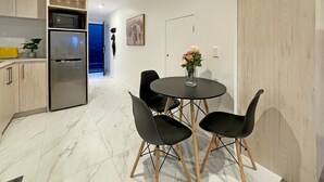 Eine moderne Küche mit integriertem Mikrowellenherd und Kühlschrank, ein Essbereich mit rundem Tisch und schwarzen Stühlen sowie ein Flur, der zu einem weiteren Raum führt.