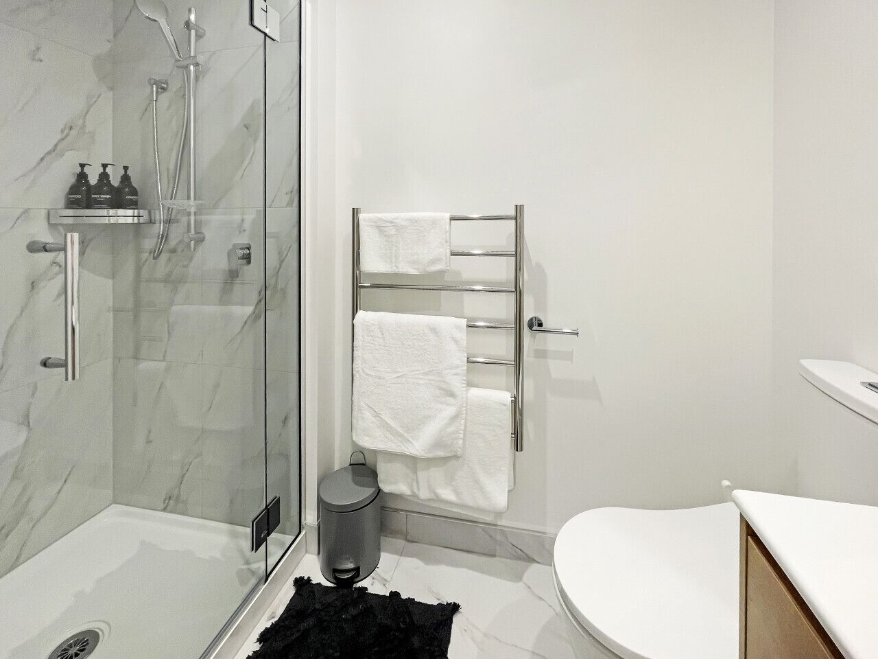 Een moderne badkamer met een douchecabine van glas, een wit toilet en een chromen handdoekrek.