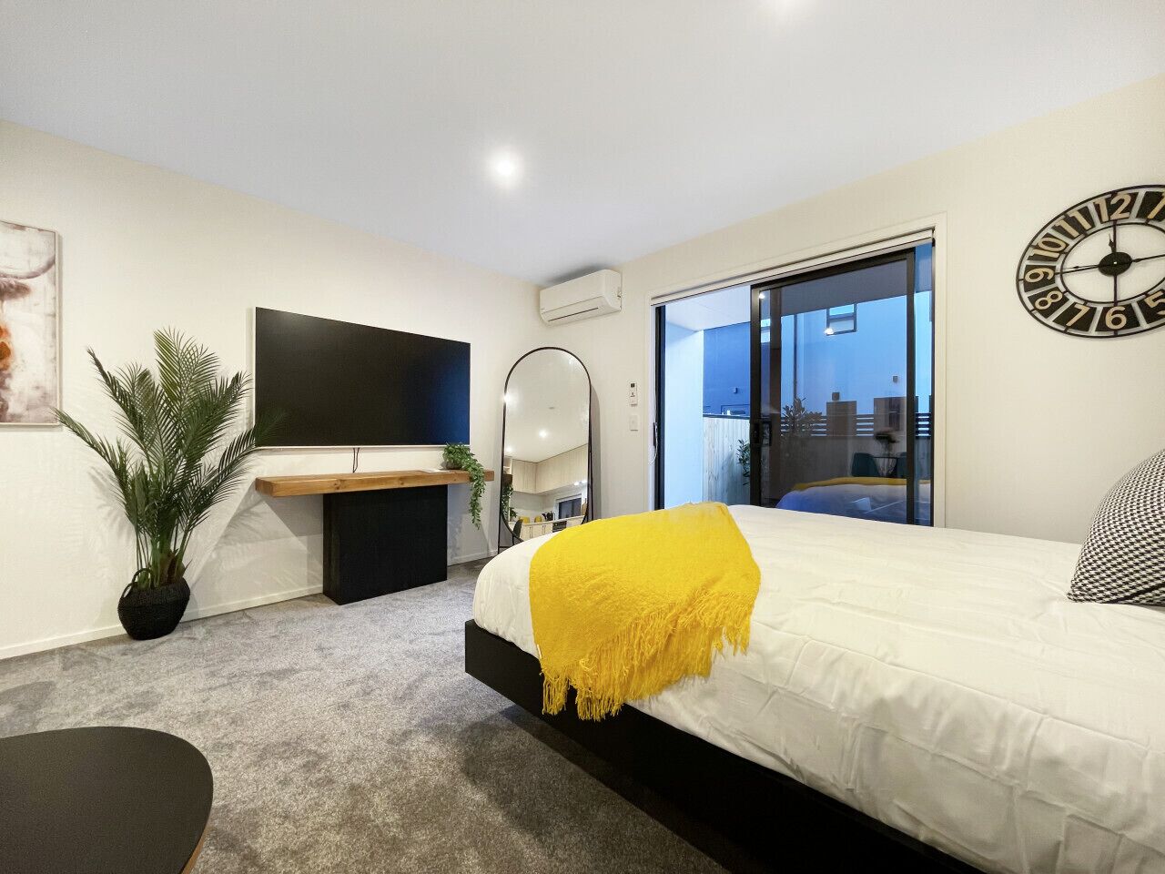 Un dormitorio moderno con cama, escritorio, televisor y un ventanal grande.