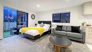 Ein modernes Schlafzimmer mit Bett, grauem Sofa, Couchtisch und Blick ins Freie.