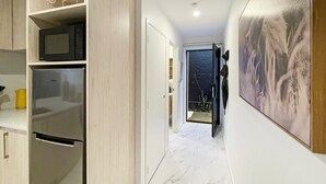 Ein Flur mit Küchenbereich, einer Tür, die auf einen Balkon führt, und einem großen abstrakten Gemälde an der Wand.