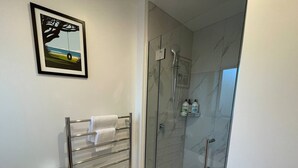 Un baño moderno con ducha de vidrio, un perchero con toallas y un cuadro en la pared.