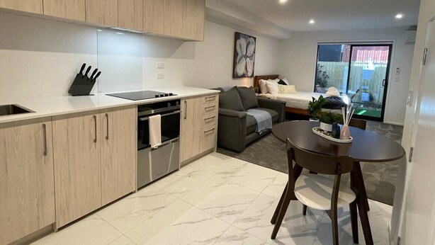 Una cocina moderna con armarios de madera clara, horno empotrado y comedor con una mesa redonda y sillas.