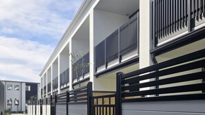 Un edificio moderno con fachada gris, portones de metal negro y un camino de hormigón.