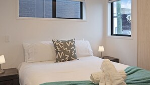 Una habitación de hotel con una cama, dos mesitas de noche, un ventanal y una manta verde.