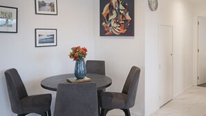 Un comedor con una mesa redonda, cuatro sillas, un florero con flores y tres cuadros en la pared.