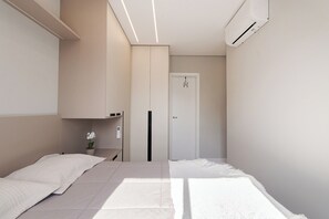 Une chambre à coucher au style minimaliste, avec deux lits, une petite table ornée d’une fleur et une porte visible au fond.