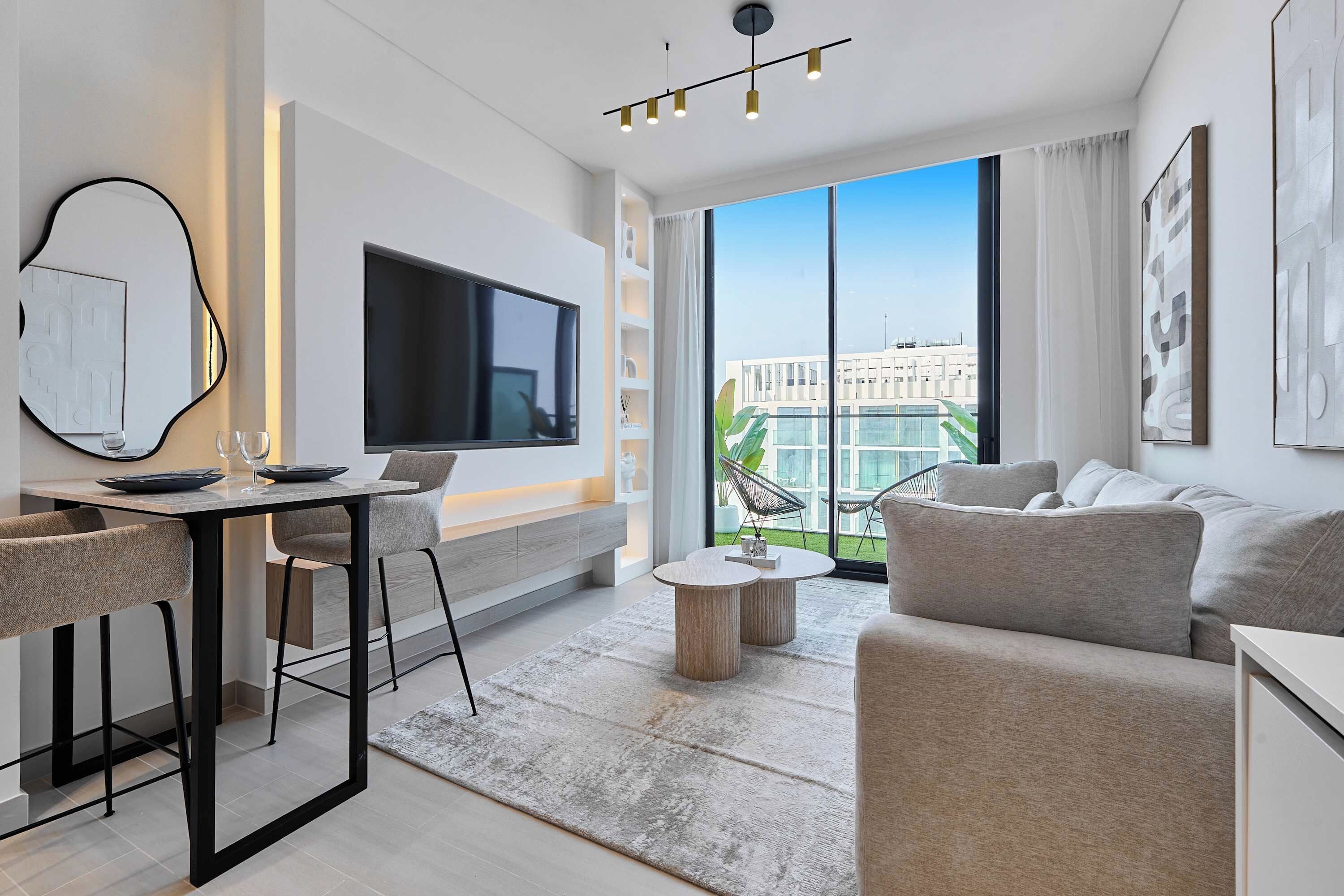 Una sala de estar moderna con una televisión de pantalla plana, un comedor con taburetes de bar, un sofá y un ventanal con vistas a la ciudad.