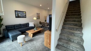 A living room with a dark grey sofa, a wooden coffee table, and a staircase with grey carpeted steps. - Modern and Contemporary 3BR Home (Christchurch)