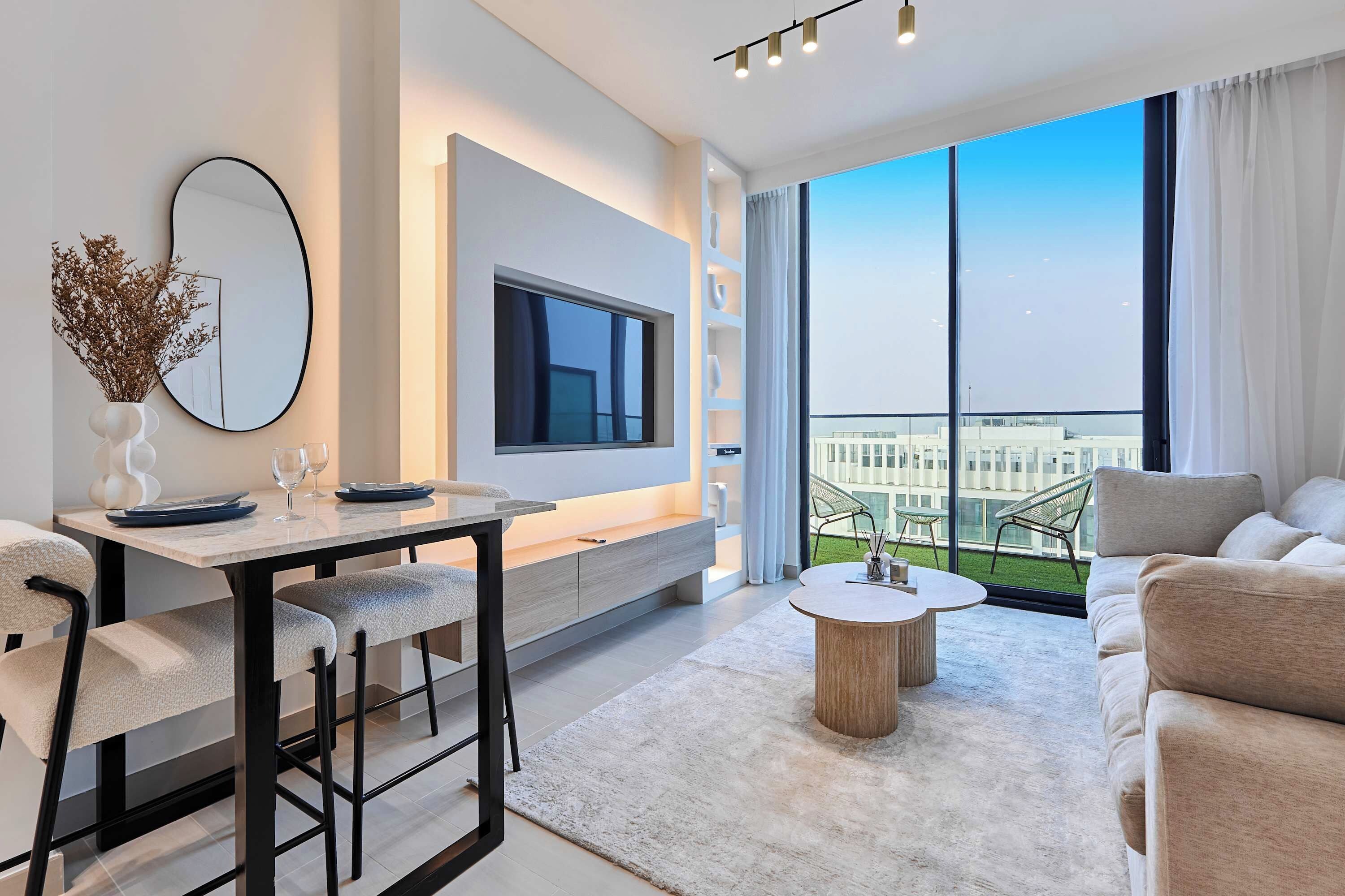 Una sala de estar moderna con comedor, televisor de pantalla plana, ventana grande con vista a la ciudad y balcón con mobiliario exterior.