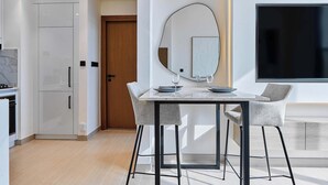 A modern kitchen with white cabinetry, a dining area with a table and chairs, a large mirror, and a flat-screen TV mounted on the wall.