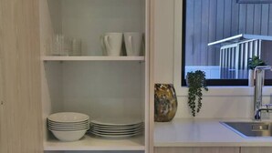 Une cuisine avec des placards ouverts où sont exposés la vaisselle, les verres et les ustensiles de cuisine.
