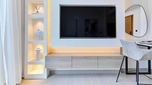 Ein modernes Wohnzimmer mit einem großen Wandfernseher, einer eingebauten Schrankwand mit Dekoration und einem grauen Sessel sowie einer hölzernen Bank.