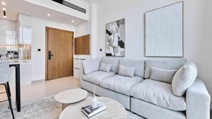 Ein modernes Wohnzimmer mit einem grauen Sofa, einem runden Couchtisch und einer Küche im Hintergrund.