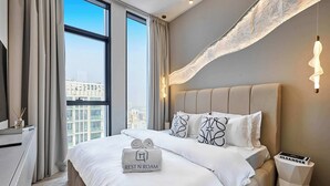 Ein modernes Hotelzimmer mit einem großen Bett, einem Nachttisch, einer Lampe und Blick auf die Stadt durch große Fenster.