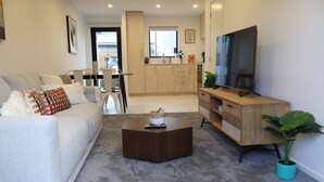 Un soggiorno moderno con un divano, un tavolino, una TV e una cucina sullo sfondo.