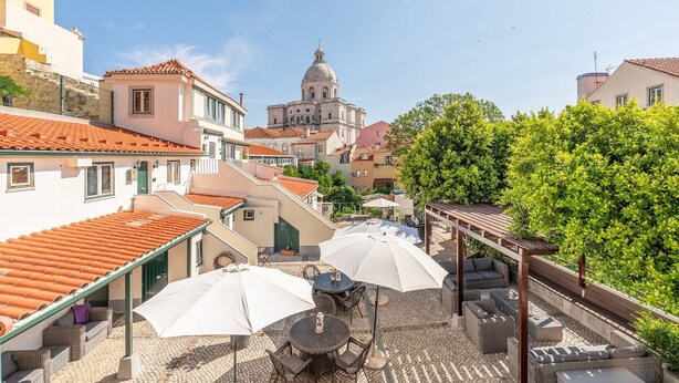 A courtyard with outdoor seating, a dome-shaped building in the background, and a tree providing shade. - GuestReady - Alfama Terrace B1 (Lisbon)