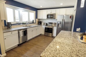 A modern kitchen with white cabinets, granite countertops, stainless steel appliances, and a large window providing natural light.