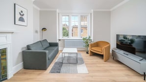 A living room with a sofa, a coffee table, a TV, a fireplace, and a window with a view of buildings.