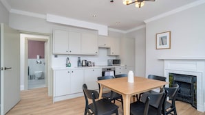 A modern kitchen with white cabinets, a wooden dining table, black chairs, a microwave, and a fireplace.