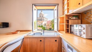 Een keuken met houten kastjes, een geïntegreerde vaatwasser en uitzicht op een historisch gebouw door een open raam.