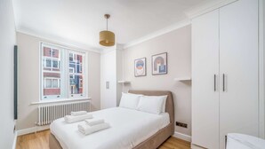 Un dormitorio moderno con una cama grande, paredes blancas y un ventanal con vistas a edificios.
