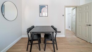 Un comedor con una mesa rectangular y cuatro sillas, un espejo redondo y una obra de arte enmarcada en la pared.