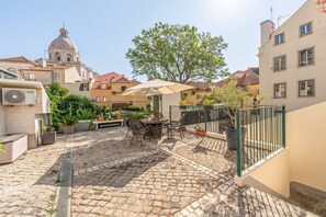 Ein Innenhof mit Tisch und Stühlen, umgeben von Kübelpflanzen und einem großen Baum.
