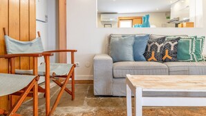 A living room with a grey sofa, wooden armchairs, a small table, and a large mirror on the wall. - GuestReady - Alfama Terrace G (Lisbon)