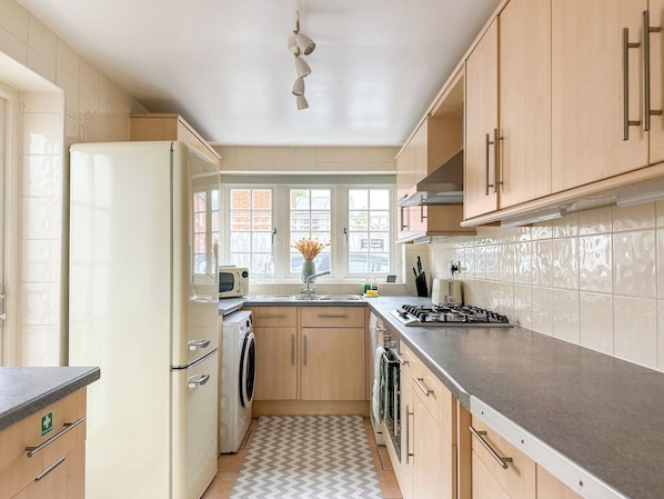 A kitchen with a refrigerator, stove, sink, and cabinets.
