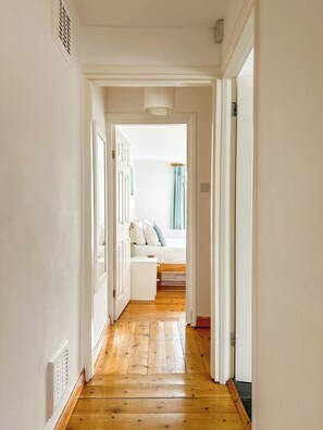Un pasillo que conduce a un dormitorio con cama, mesita de noche y ventana con cortinas.