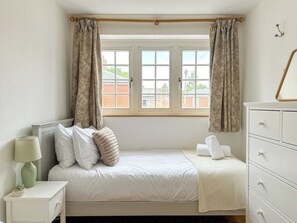 A bedroom with a bed, a nightstand with a lamp, a dresser, and a window with curtains.