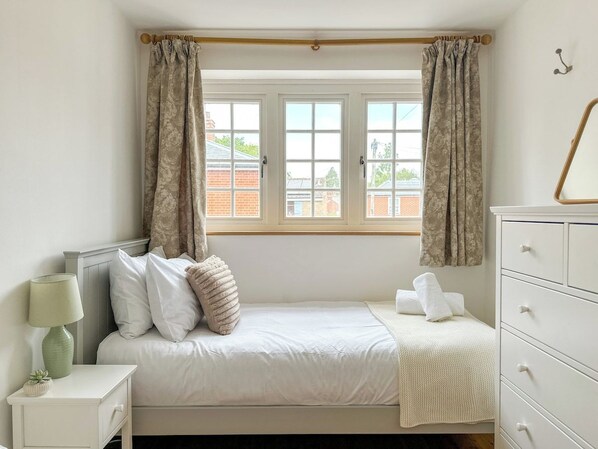 A bedroom with a bed, a nightstand with a lamp, a dresser, and a window with curtains.
