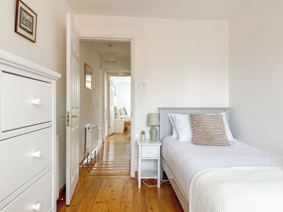 A bedroom with a bed, bedside table, lamp, and a dresser.