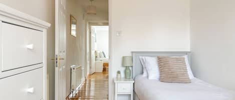 A bedroom with a bed, bedside table, lamp, and a dresser.