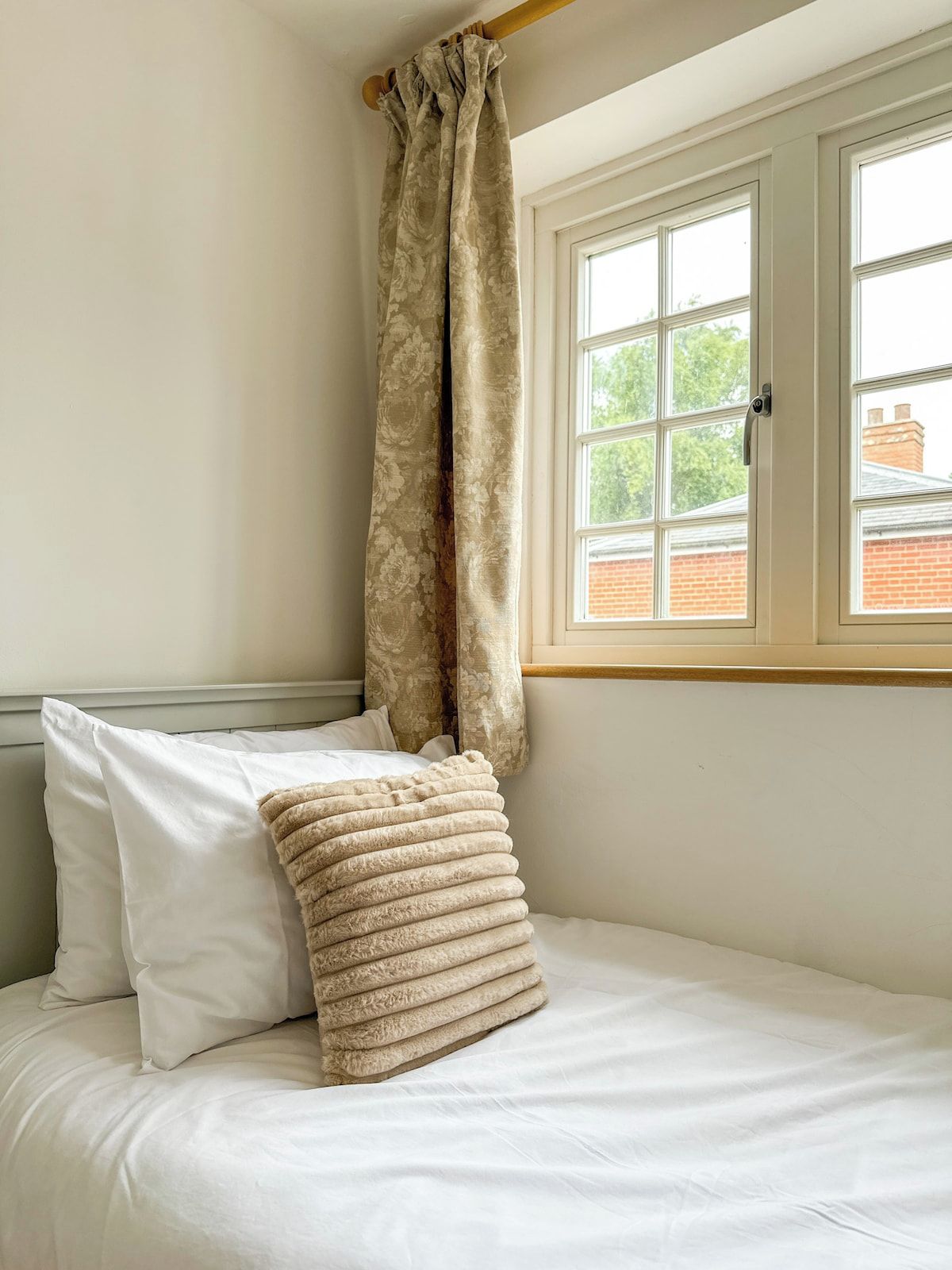 Une chambre à coucher avec un lit, du linge de lit blanc, une fenêtre donnant sur des immeubles et un rideau.