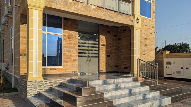 A two-story building with a stone facade, large windows, and a set of marble steps leading to a glass door. - JR KISASA HOTEL (Dodoma)
