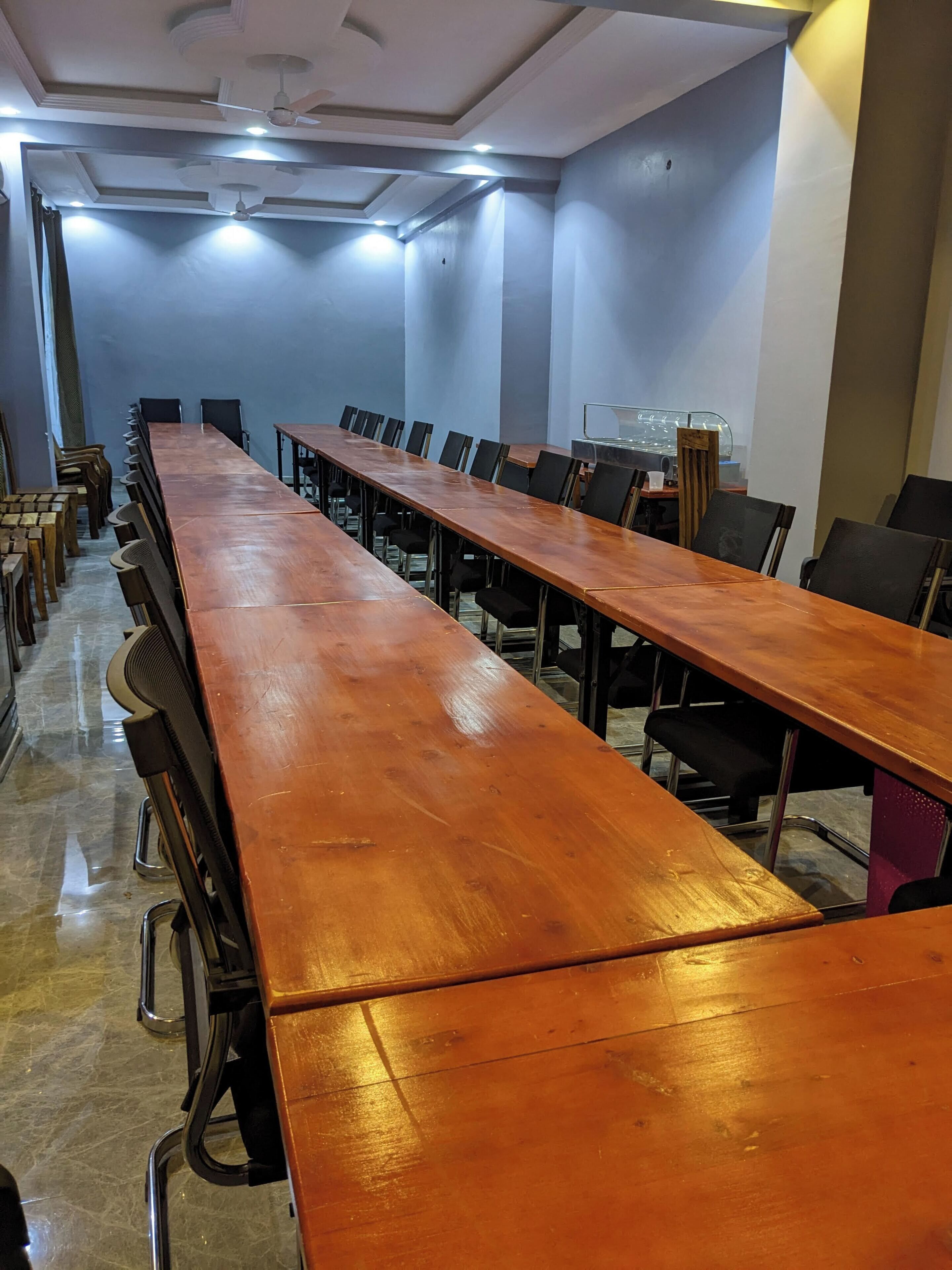 A conference room with long tables and chairs, a ceiling with recessed lighting, and a marble floor.
