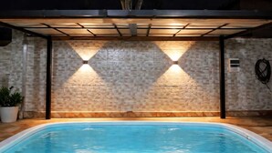 A swimming pool with a stone wall and two wall-mounted lights. - House with Heated Pool - Perequê-Açu - UBATUBA - SP (Perequê-Acu Ubatuba)