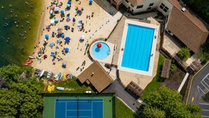 Vue aérienne d’une zone de plage avec une piscine, un court de tennis et un bâtiment doté d’un toit.