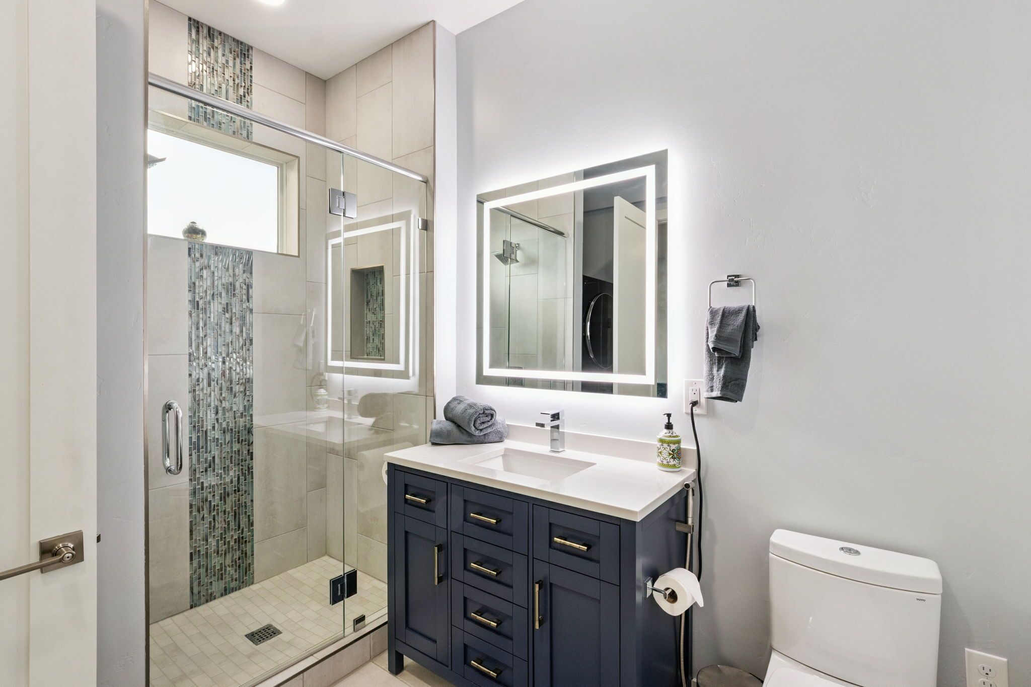 Een moderne badkamer met een douche met glazen wand, een wastafel met spiegel en een toilet.