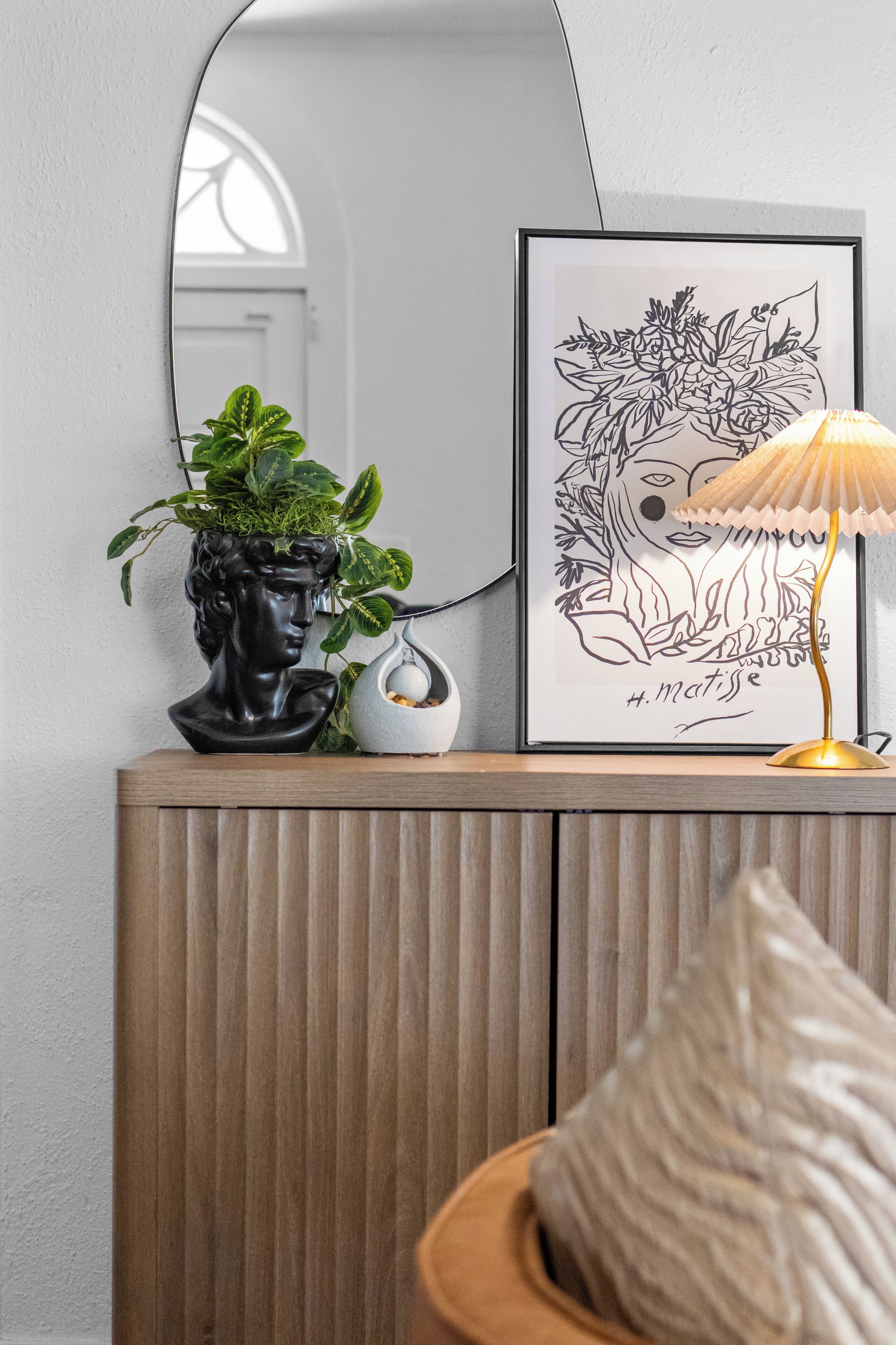 A wooden console with a potted plant, a framed artwork, and a lamp.
