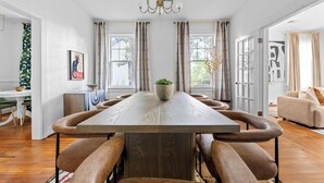 Een eetruimte met een lange houten tafel, met kussens uitgeruste banken en een kroonluchter.