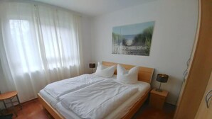 Een slaapkamer met een houten bed, wit beddengoed, een schilderij aan de muur en een tafeltje met een lamp.