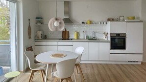 Eine moderne Küche mit weißen Schränken, einem eingebauten Ofen und einem Essbereich mit rundem Tisch und Stühlen.