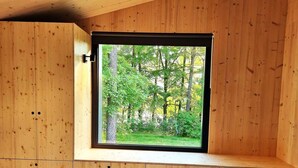 Een kamer met houten wanden en een raam met uitzicht op een bos.