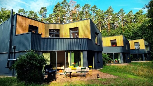 Een modern huis met twee verdiepingen, een plat dak, grote ramen en een patio met tuinmeubilair.